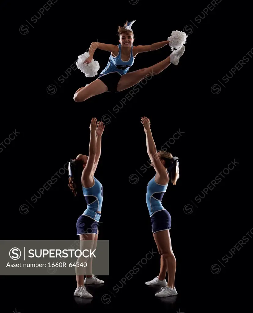 Studio shot of cheerleaders (16-17) assisting friend during jump