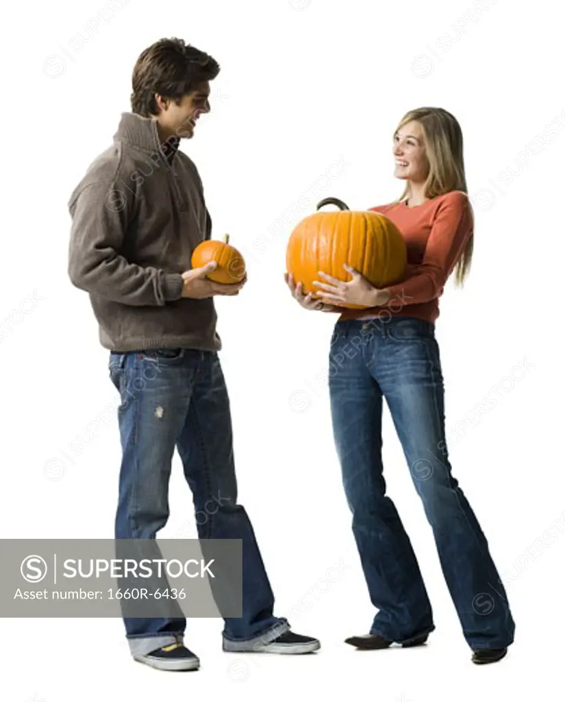 Young couple standing face to face holding pumpkins