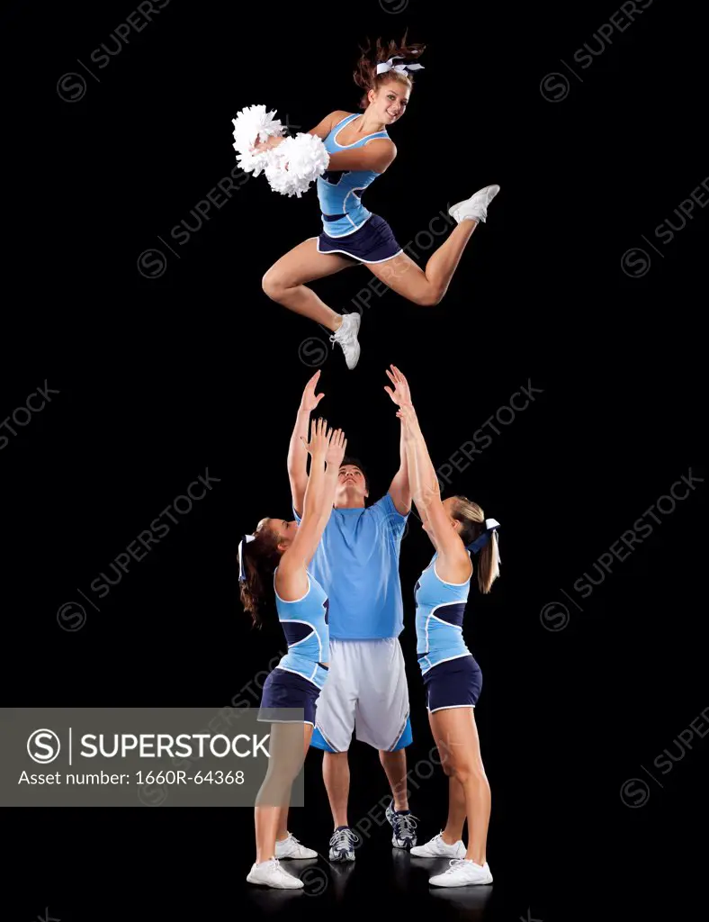 Studio shot of cheerleaders (16-17) assisting friend during jump
