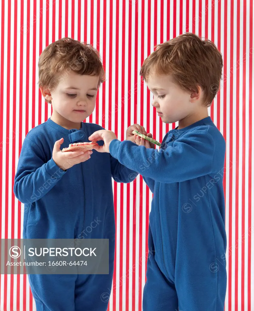 Twin boys (2-3) wearing pajamas holding gingerbreads