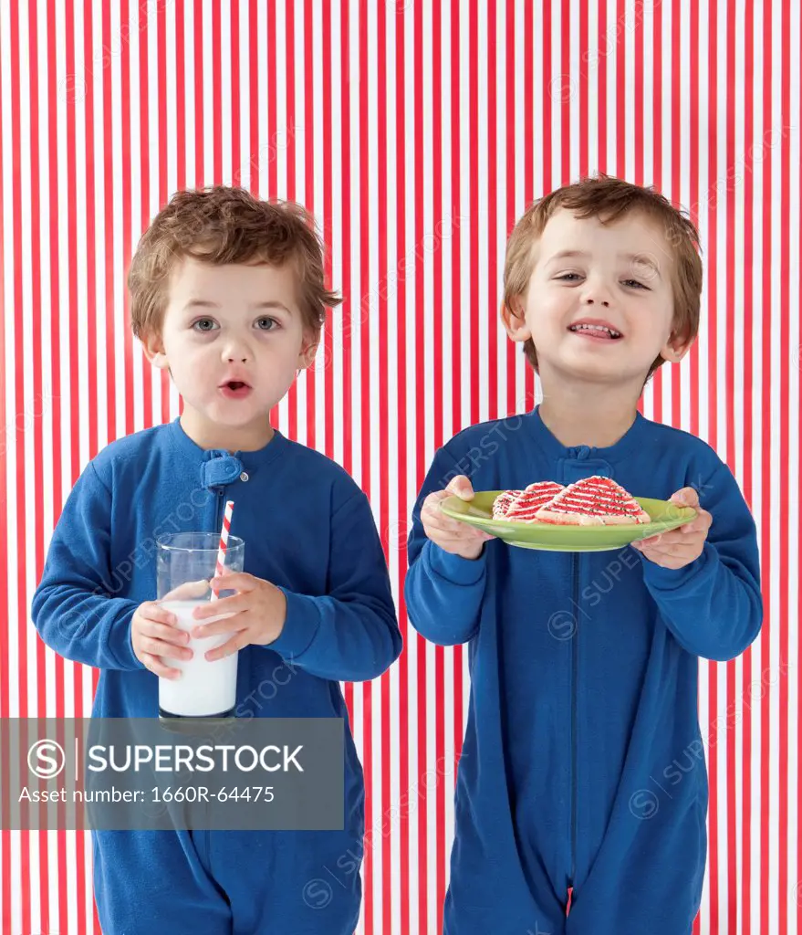 Twin boys (2-3) wearing pajamas holding gingerbreads and glass of milk