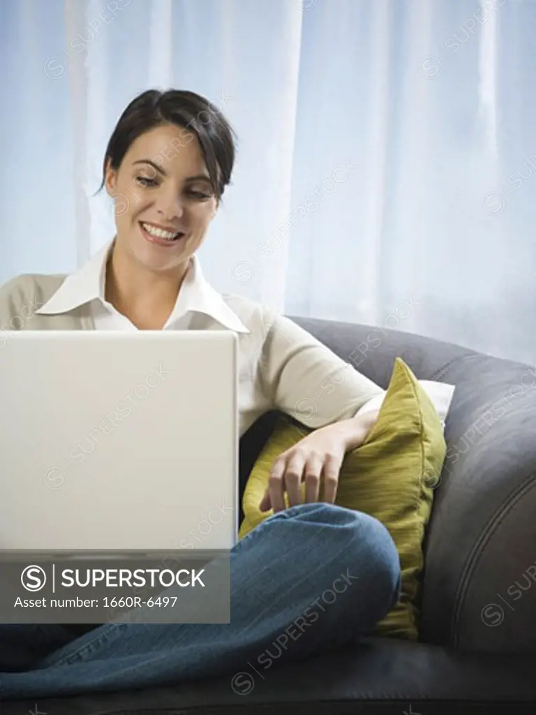 Mid adult woman sitting on a couch working on a laptop