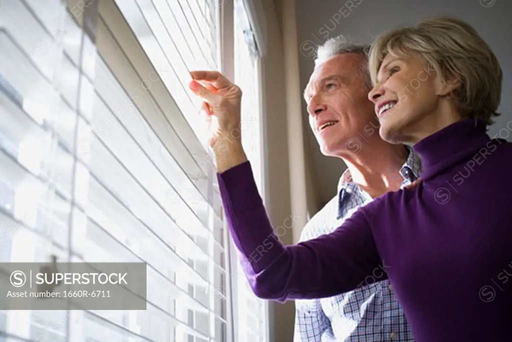 Low angle view of a mature couple looking through blinds of a window