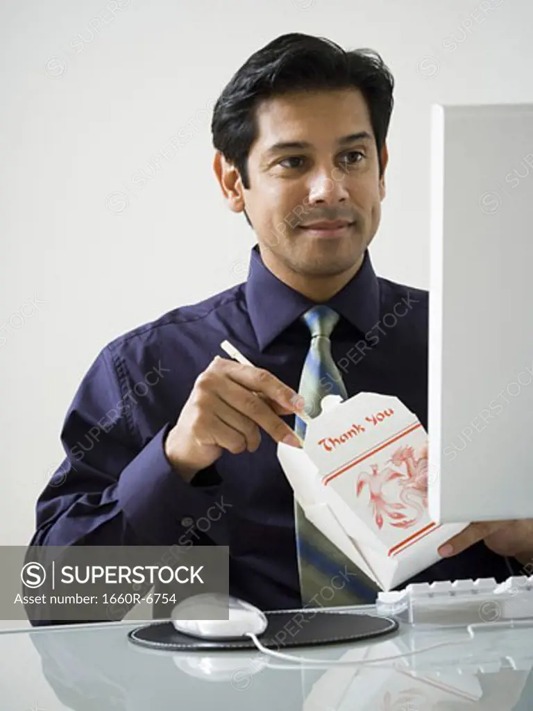 Mature man holding Chinese take away food and sitting in front of a computer