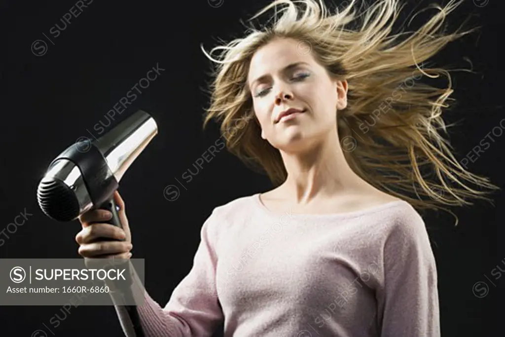 Close-up of a young woman blow drying her hair