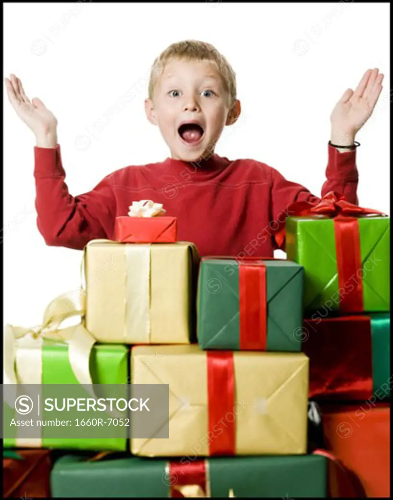 Portrait of a boy standing behind the stack of gifts with his arms raised