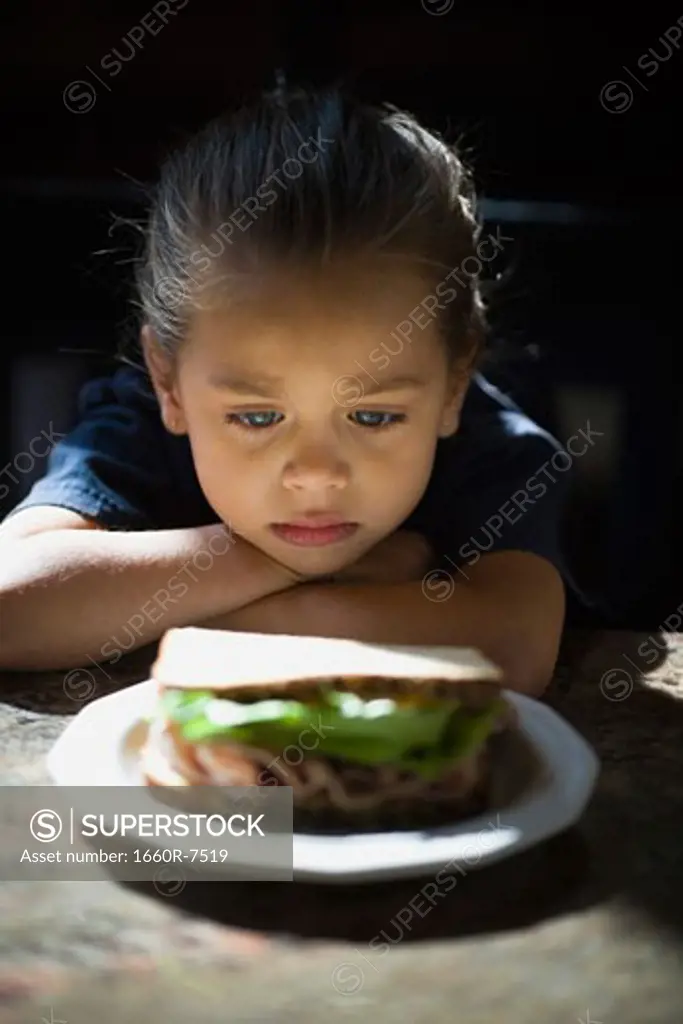 Close-up of a girl looking at a sandwich in a plate