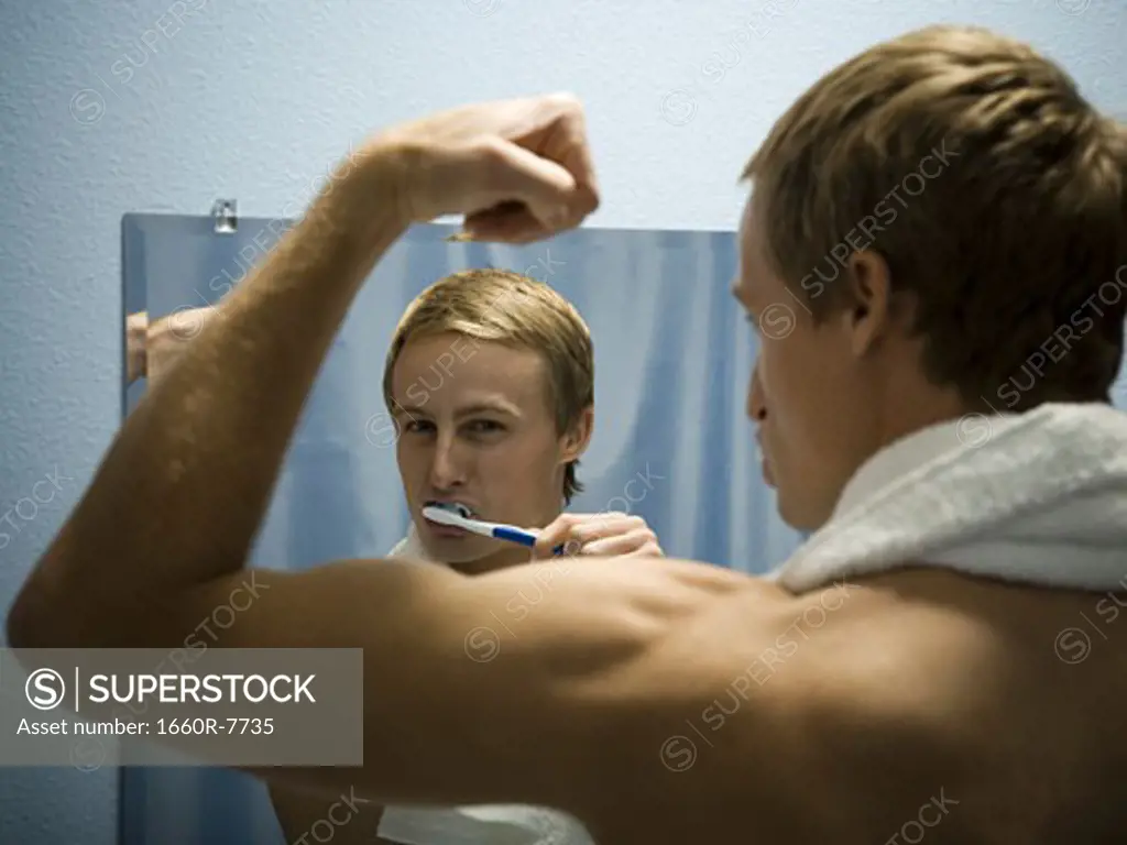 Rear view of a young man brushing his teeth and flexing his biceps