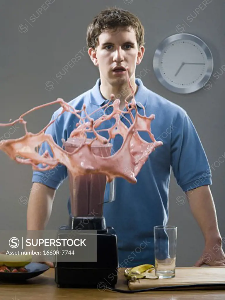 Portrait of a young man standing in front a blender splashing a smoothie