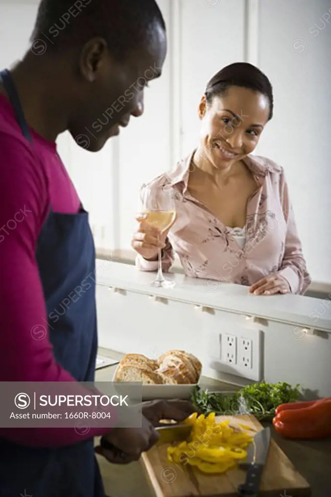 Woman holding a glass of white wine talking to man preparing dinner