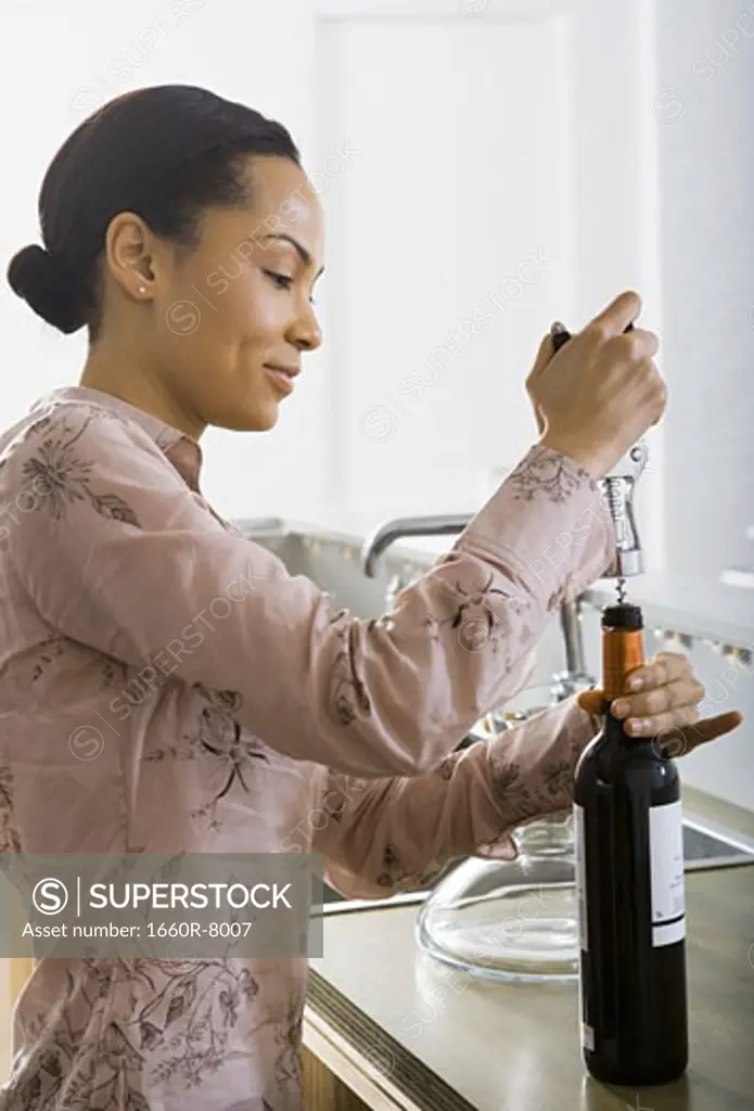 Profile of a young woman unscrewing the cork of a wine bottle