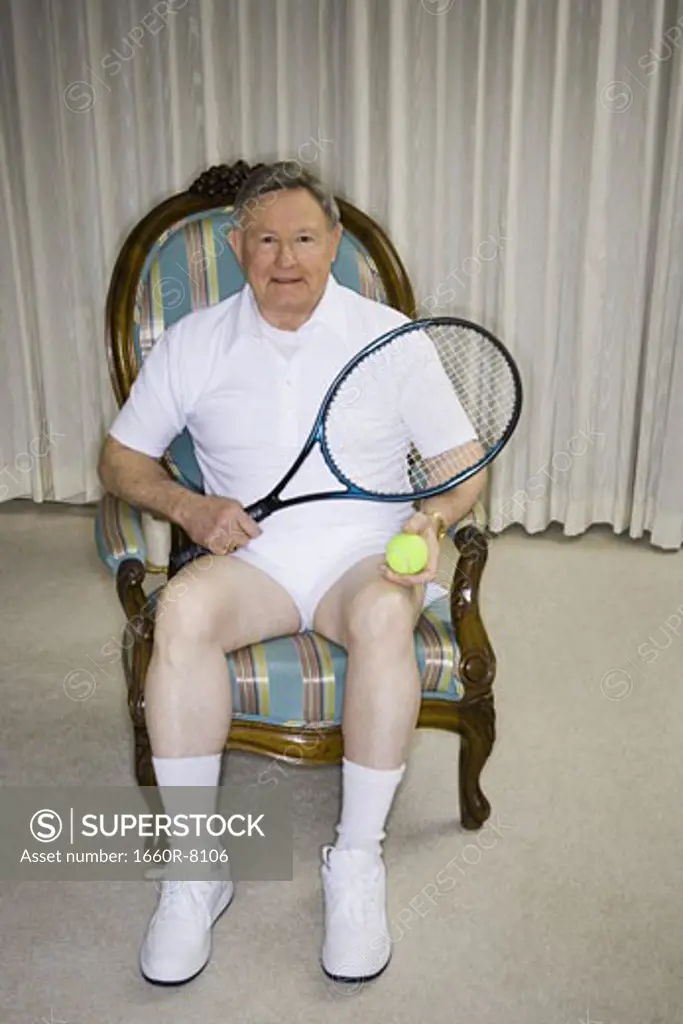 Portrait of a senior man sitting on a chair holding a tennis racket and a tennis ball