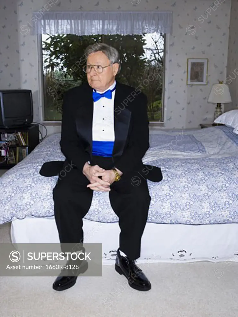 Senior man in tuxedo sitting on bed