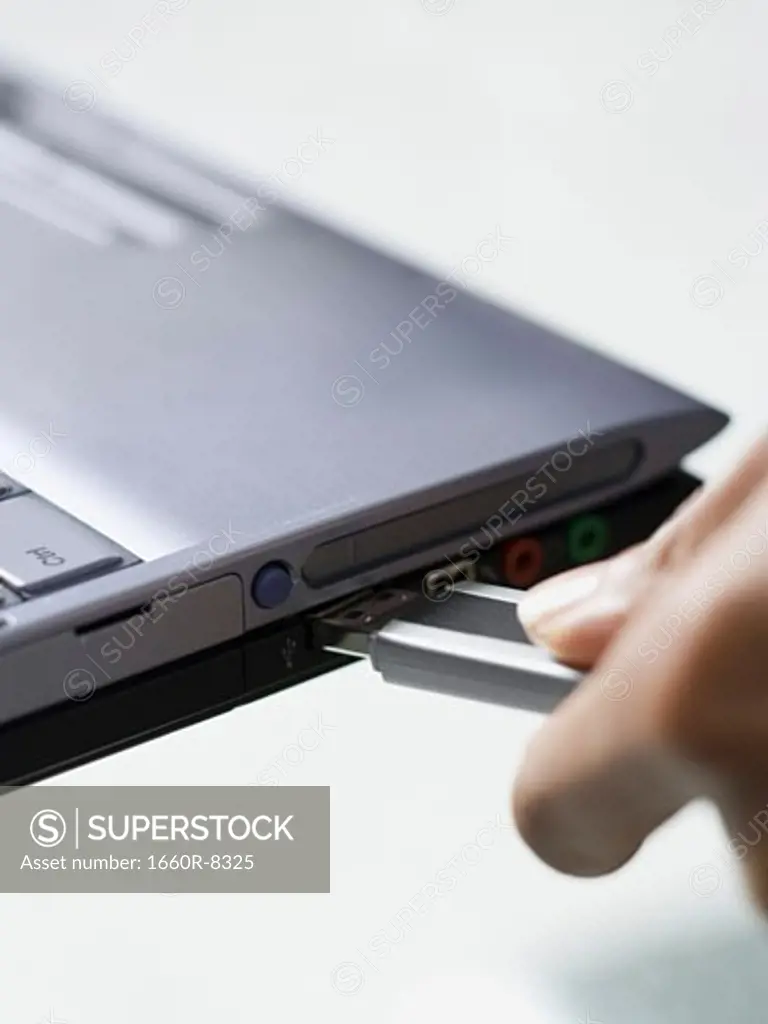 Close-up of a person's hand connecting a jump drive to a laptop