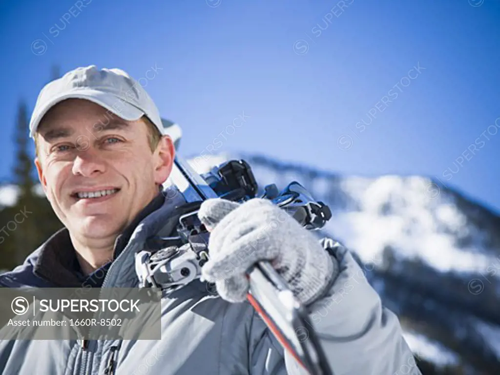 Portrait of an adult man holding skis on his shoulder