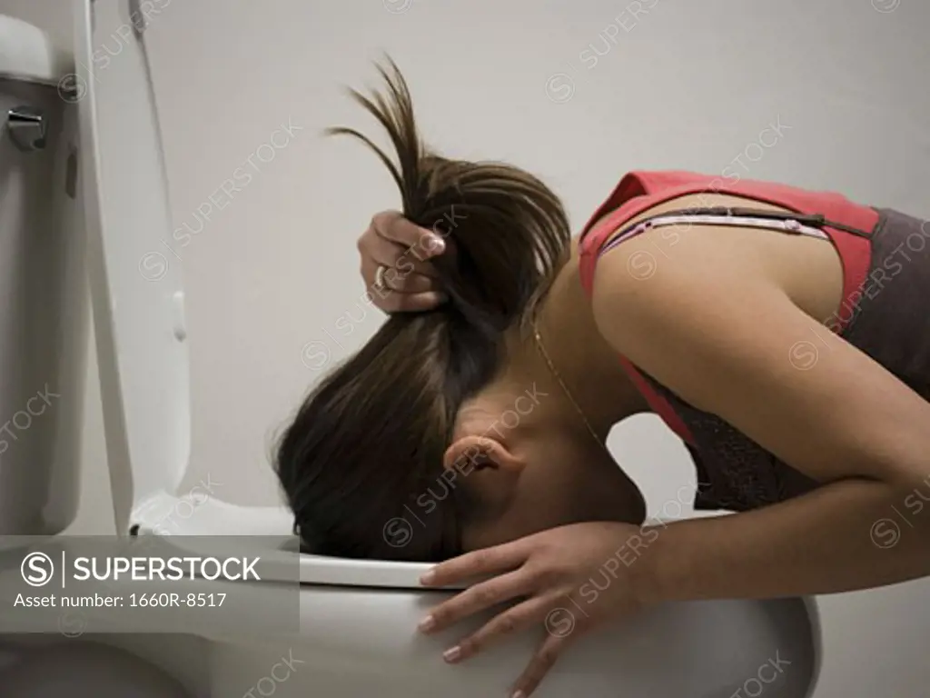 Profile of a young woman vomiting into a toilet bowl