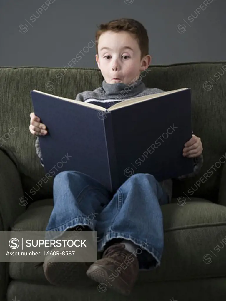 Close-up of a boy reading a book and making a face