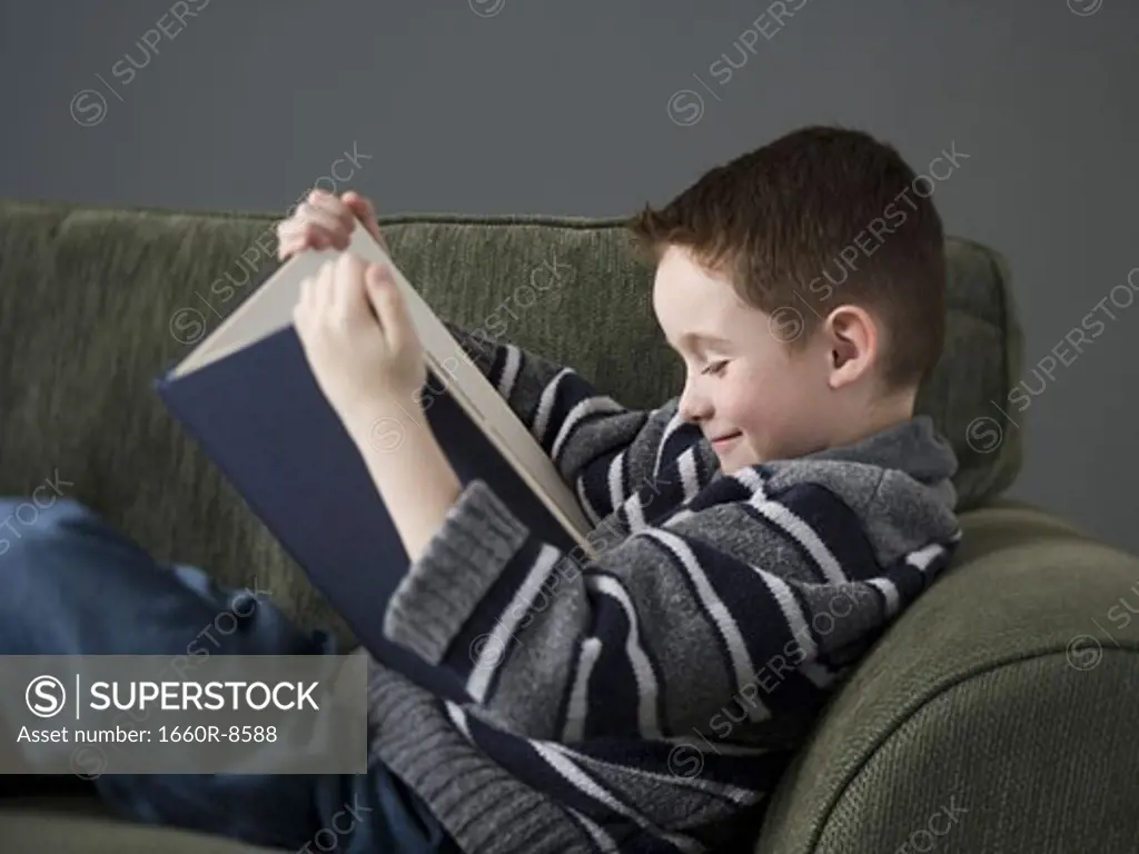 Profile of a boy reading a book on a couch