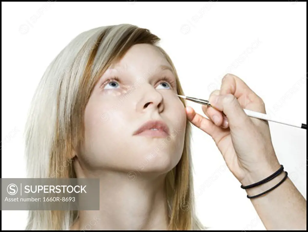 Close-up of a person's hand applying eyeliner on a young woman's eyes