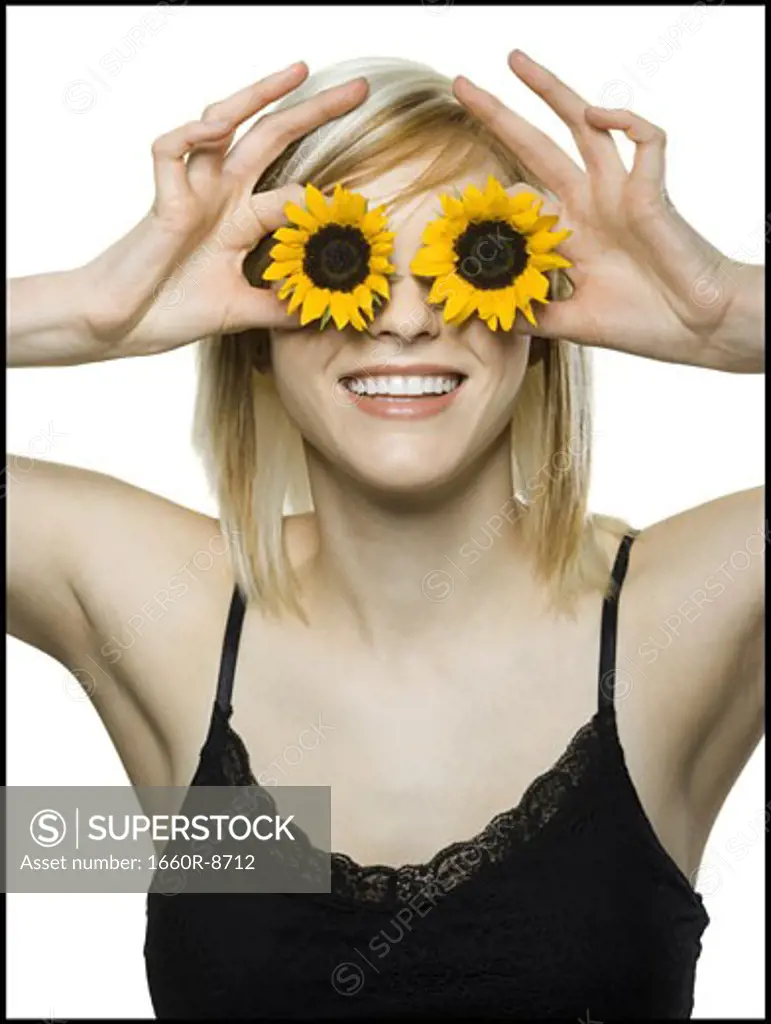 Close-up of a young woman holding sunflowers in front of her eyes