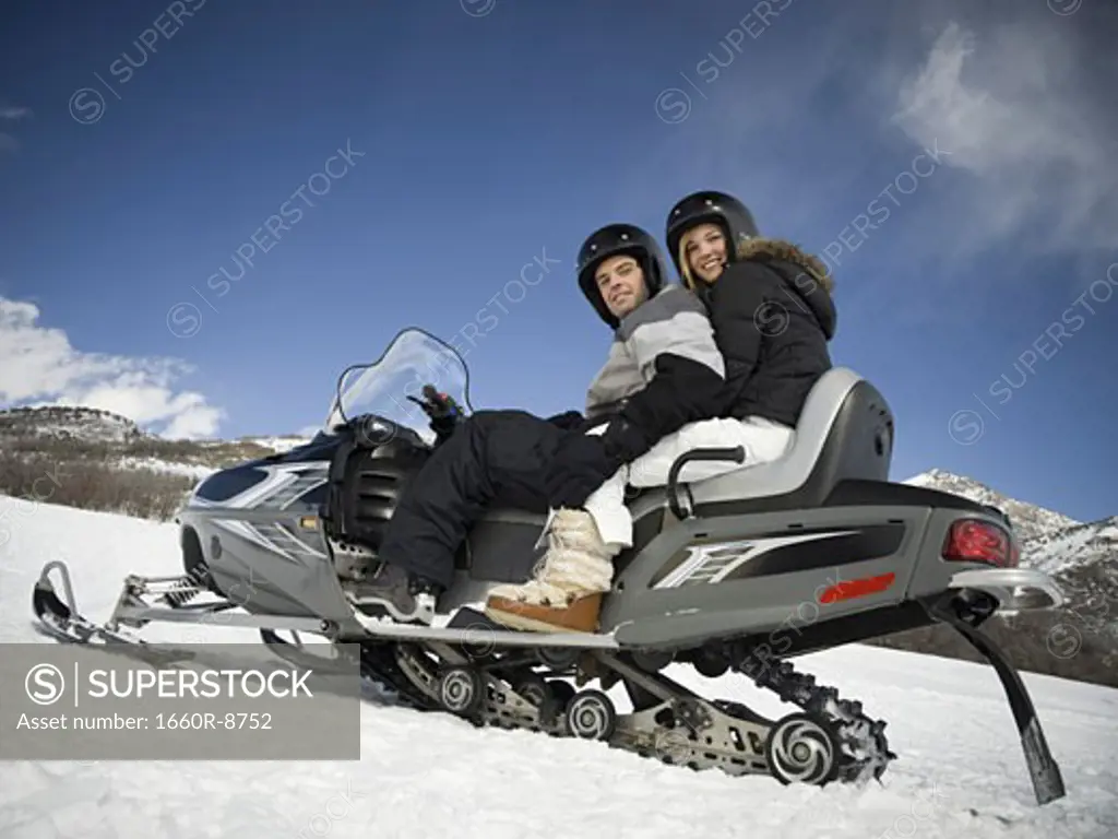 Low angle view of a young couple sitting on a snowmobile