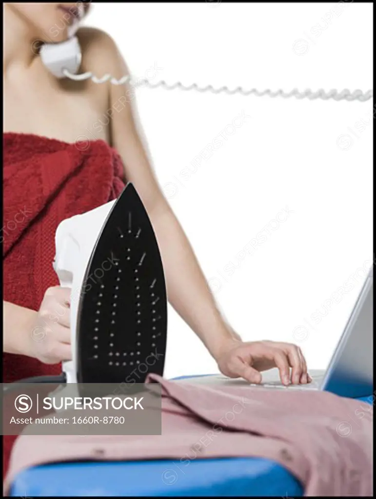Close-up of a young woman talking on the telephone while ironing