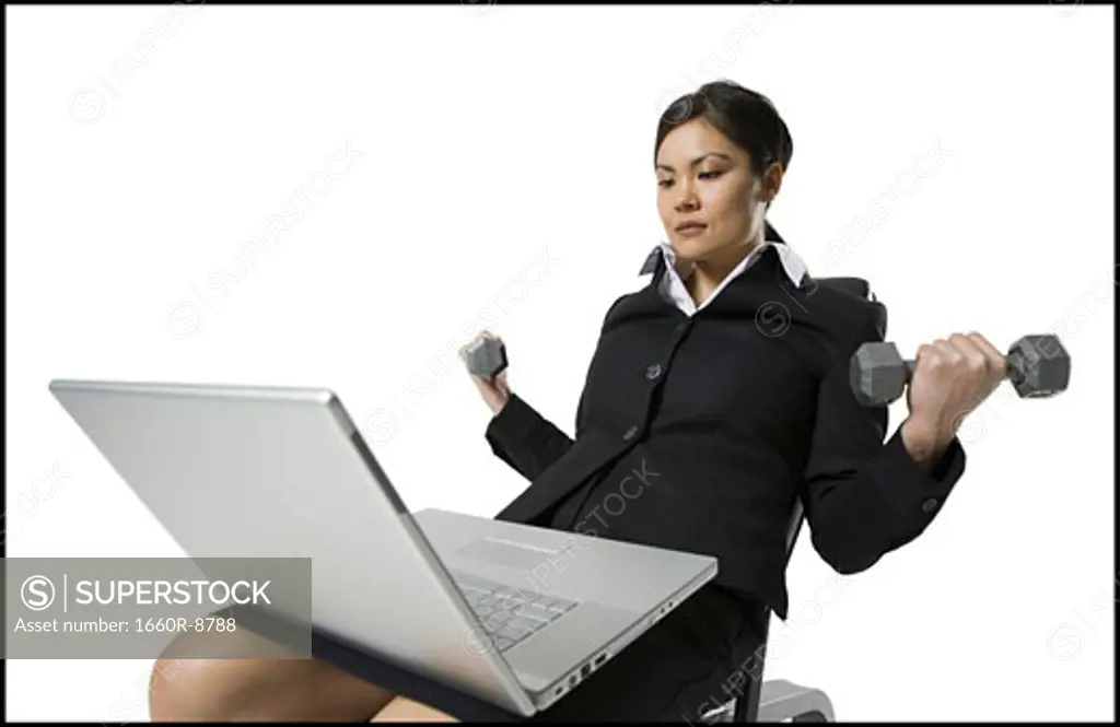 Businesswoman exercising with dumbbells while working on a laptop