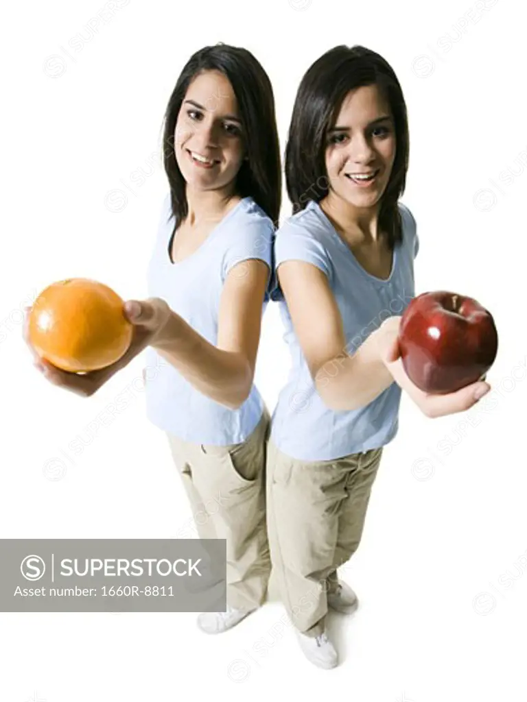 High angle view of two teenage girls holding an apple and an orange