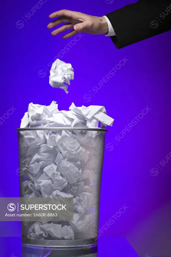 Close-up of a businessman's hand throwing a paper ball into a garbage bin