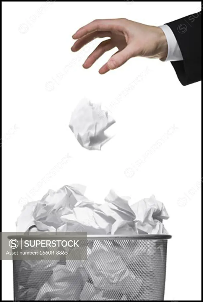 Close-up of a businessman's hand throwing a paper ball into a garbage bin