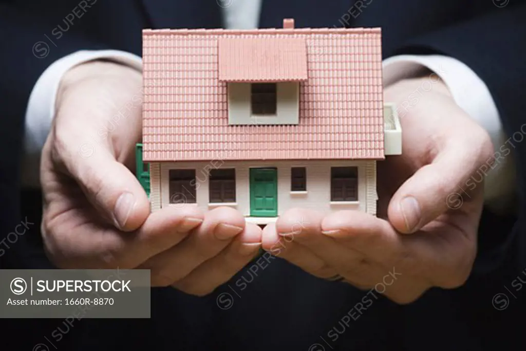 Mid section view of a businessman holding a model house in his hands