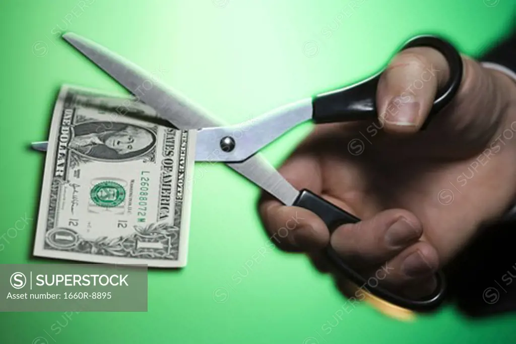 Close-up of a person's hand holding a pair of scissor cutting a one dollar bill