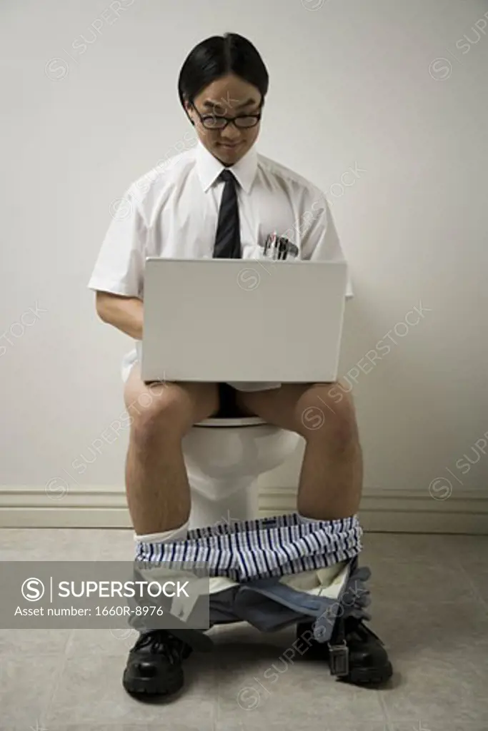 Close-up of a young man sitting on a toilet using a laptop