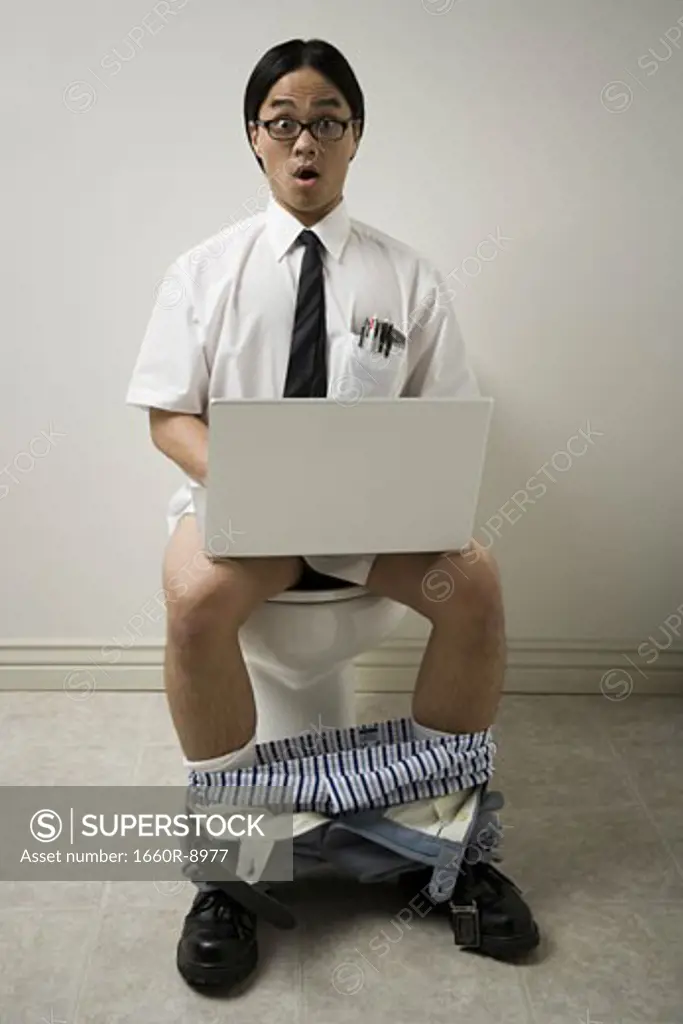 Portrait of a young man sitting on a toilet using a laptop