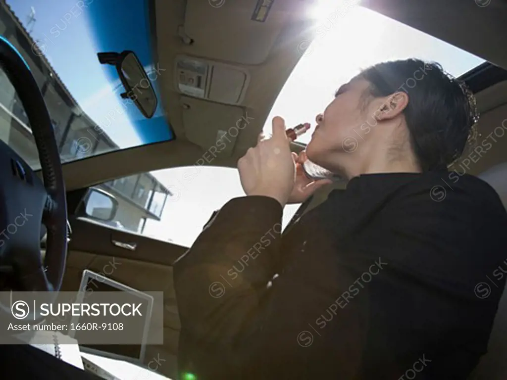 Low angle view of a businesswoman applying lipstick while talking on a mobile phone in a car