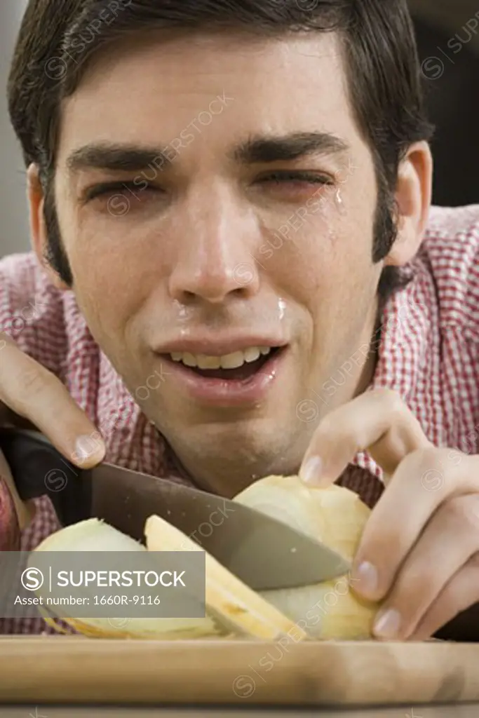 Close-up of a young man with tears in his eyes while cutting onions