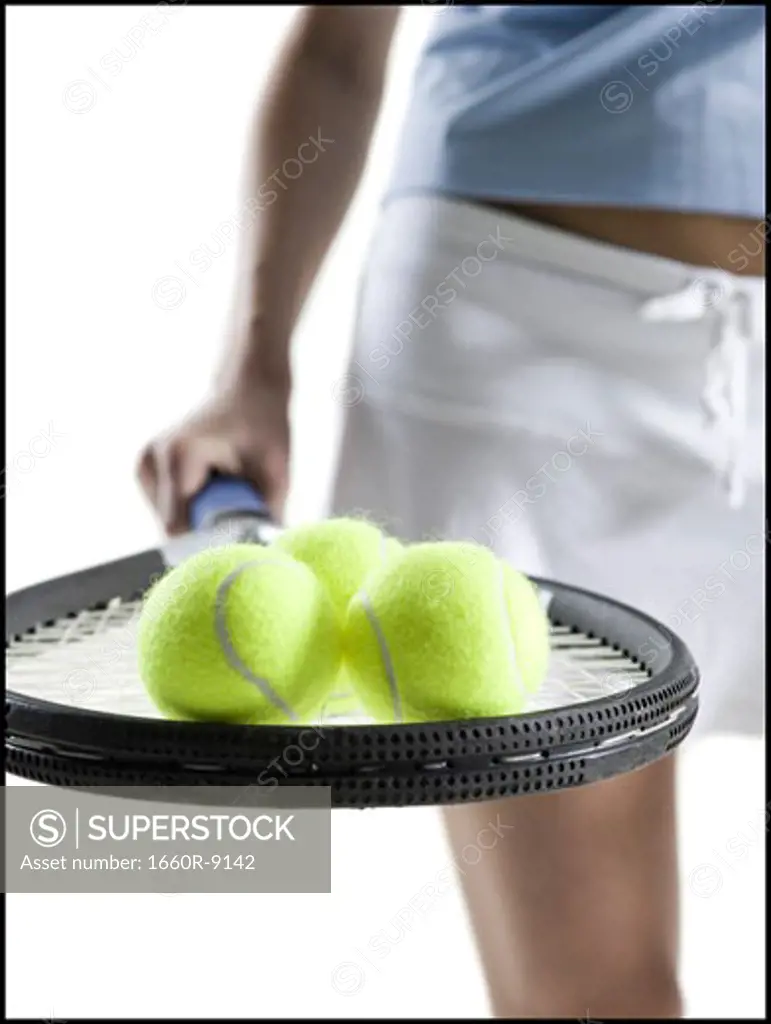 Mid section view of a young woman holding a tennis racket with three tennis balls
