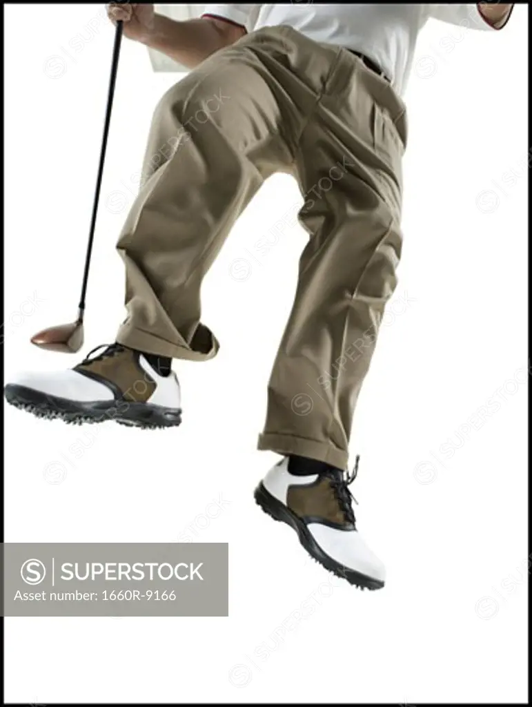 Low section view of a mid adult man jumping with a golf club