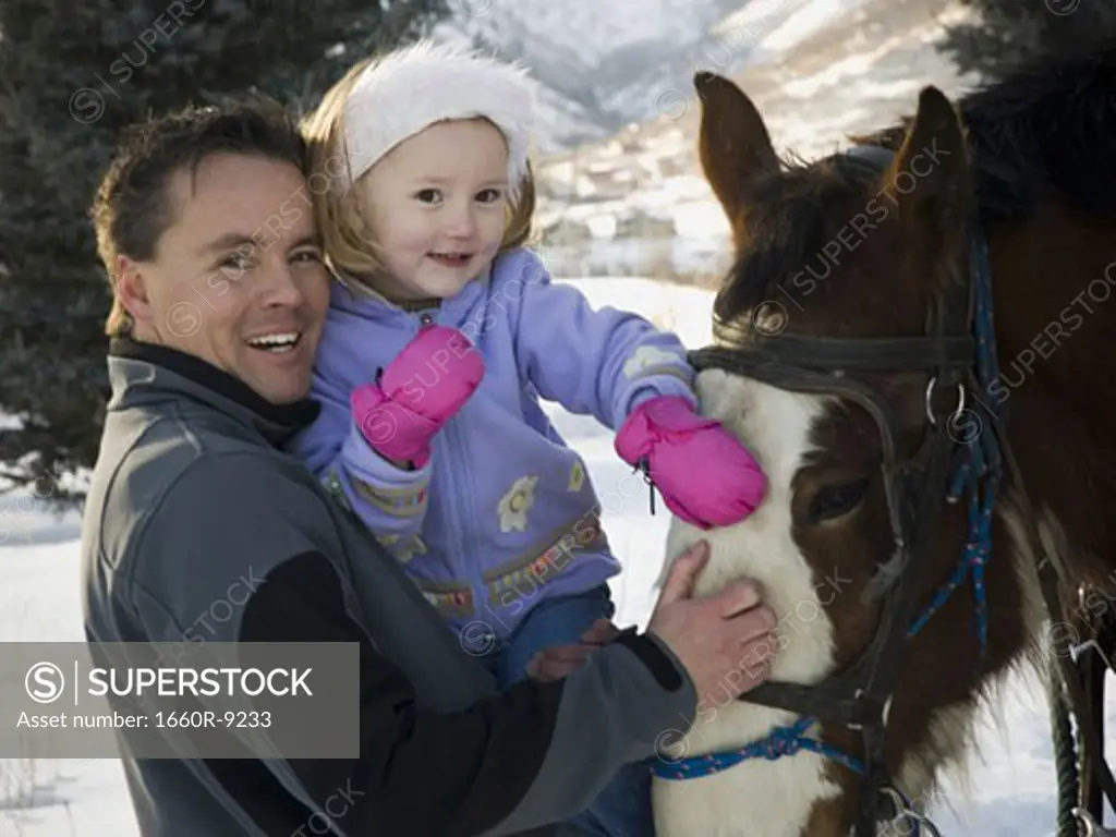 Close-up of a mid adult man and his daughter standing beside a horse