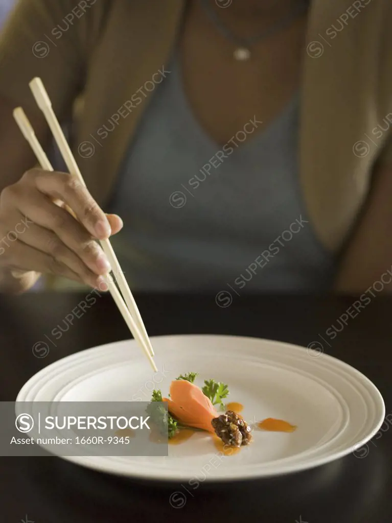 Mid section view of a woman eating food with a pair of chopsticks