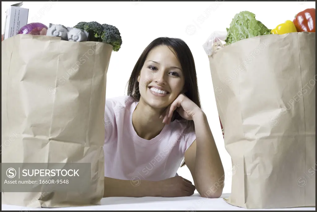 Portrait of a young woman sitting between two paper bags of vegetables
