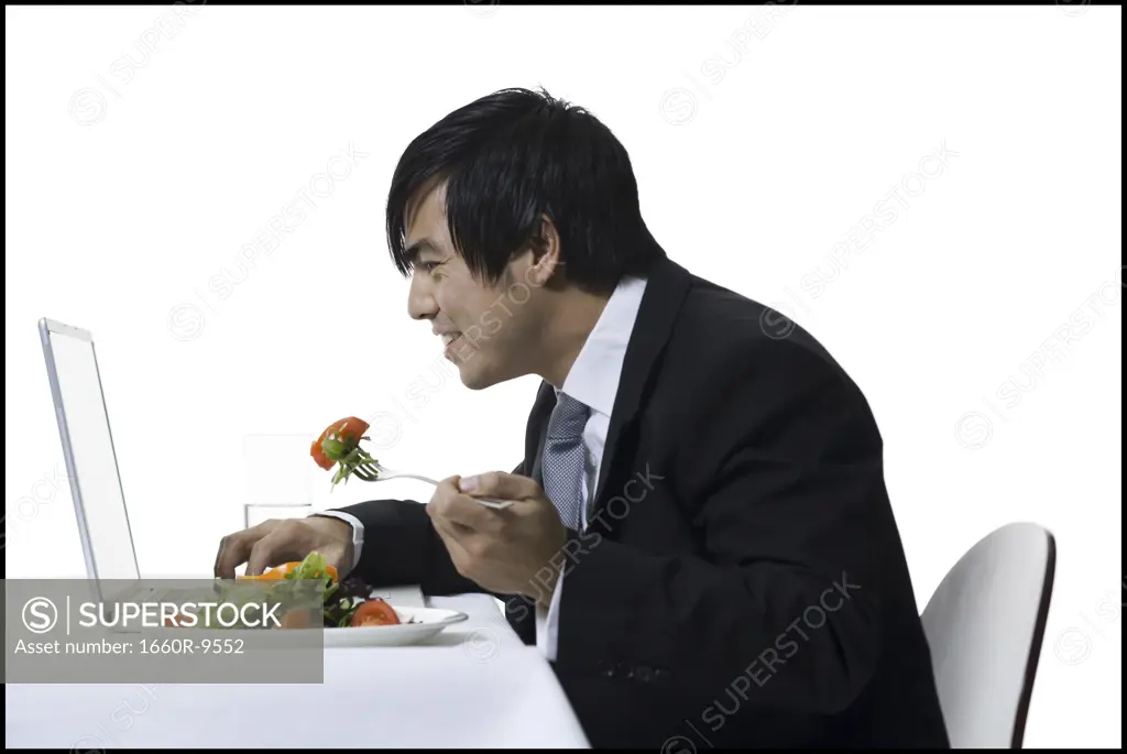 Profile of a businessman eating while using a laptop