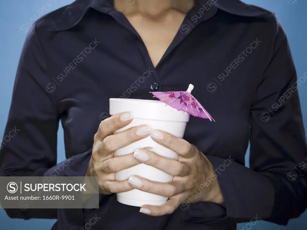 Mid section view of a young woman holding cup with a decorativ e drink umbrella
