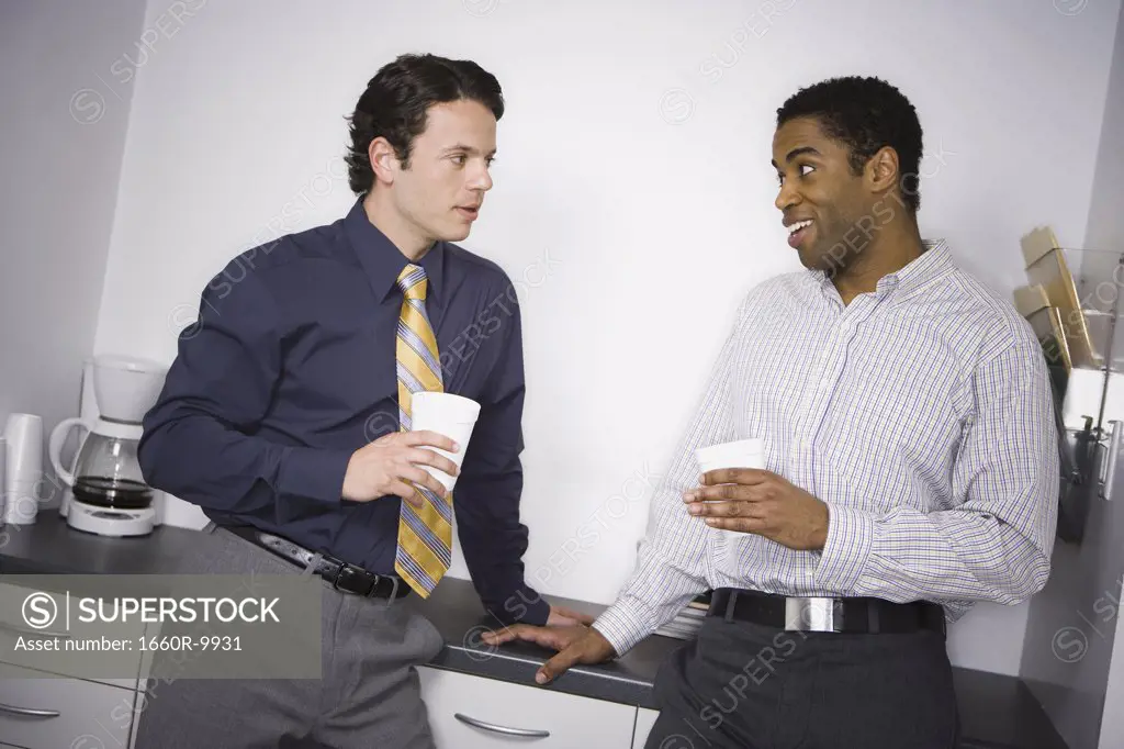 Close-up of two businessmen leaning against a drawer and looking at each other