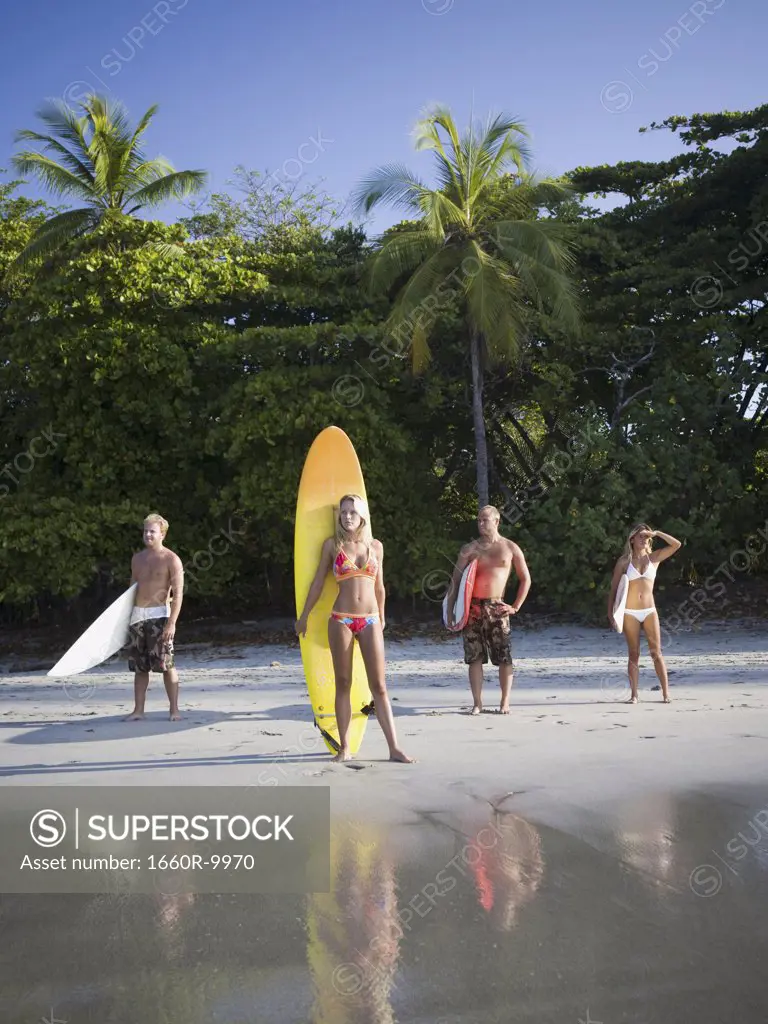 Mid adult couple and a young couple standing on the beach with surfboards