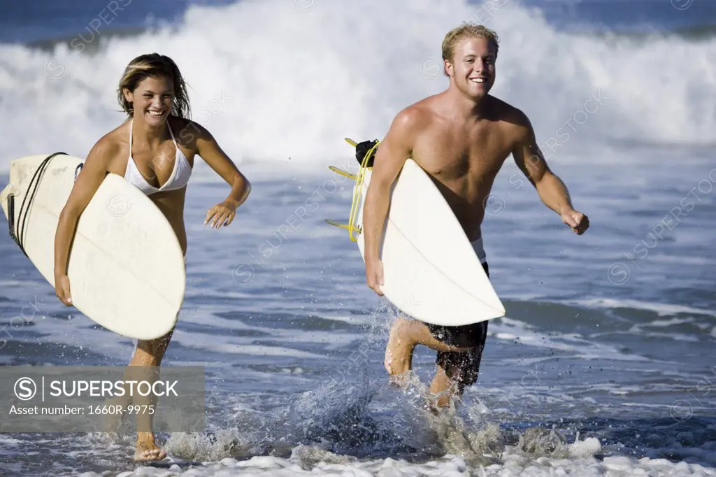 Young couple carrying surfboards and running in water