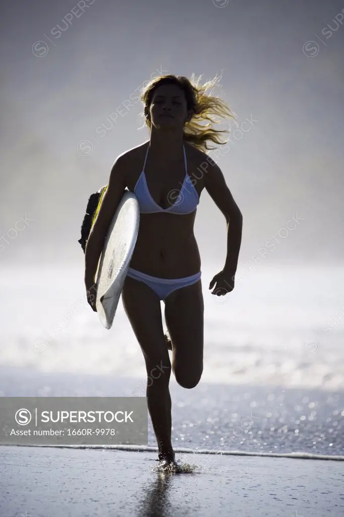 Young woman running on the beach with a surfboard