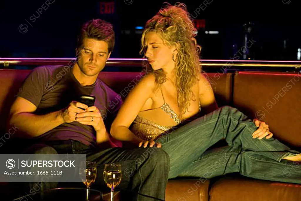 Close-up of a young man using a mobile phone with a young woman sitting beside him