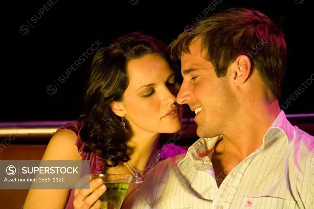 Close-up of a young woman sitting with a young man in a nightclub and holding a cocktail
