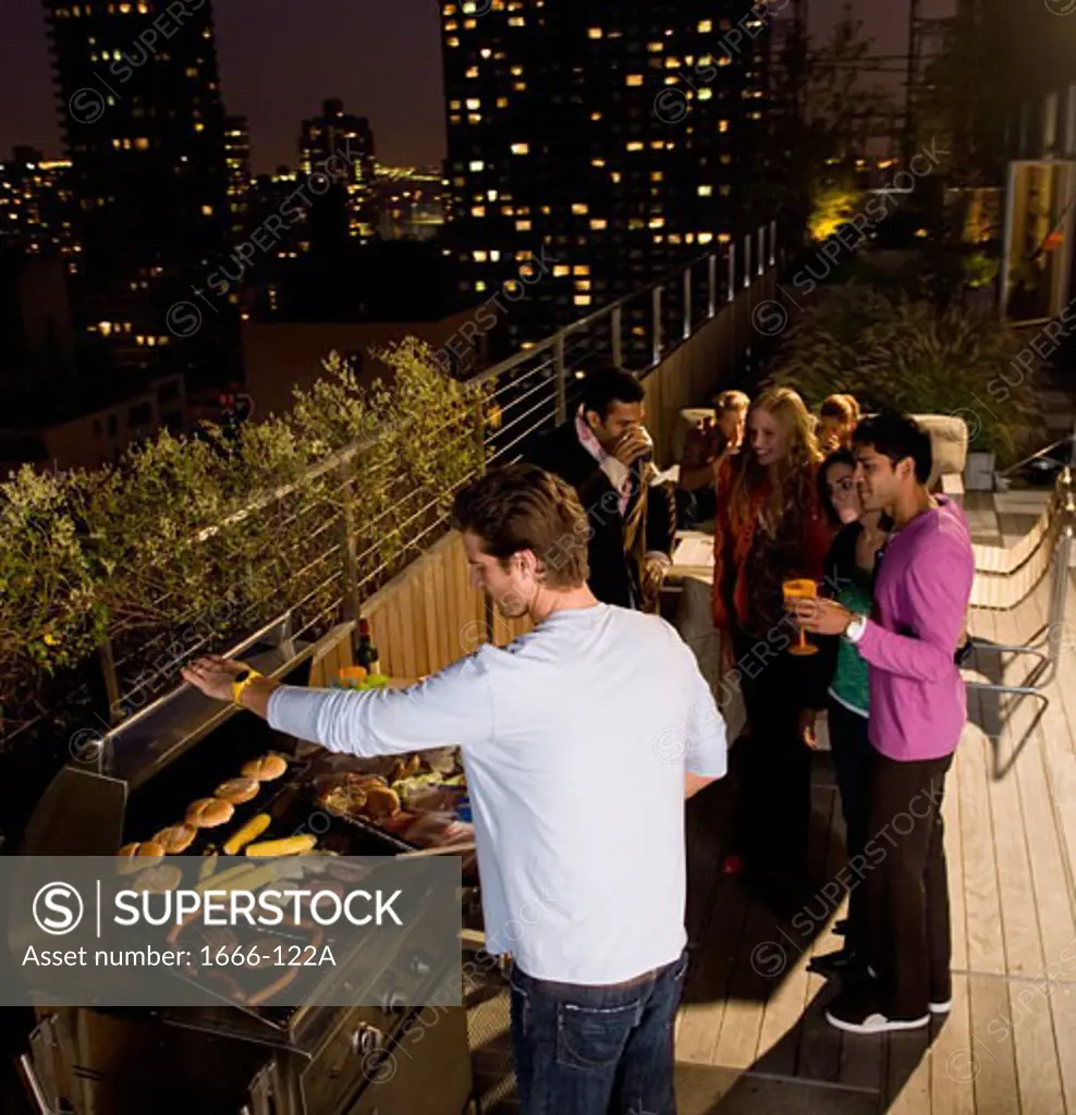 Young man grilling with mid adult men and young women watching